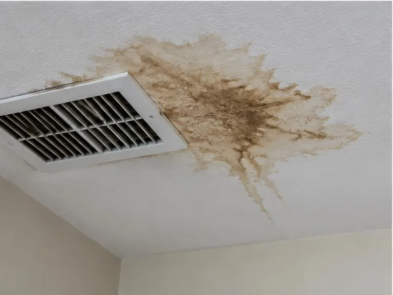 Brown water stain on a ceiling beside an air-conditioning vent.