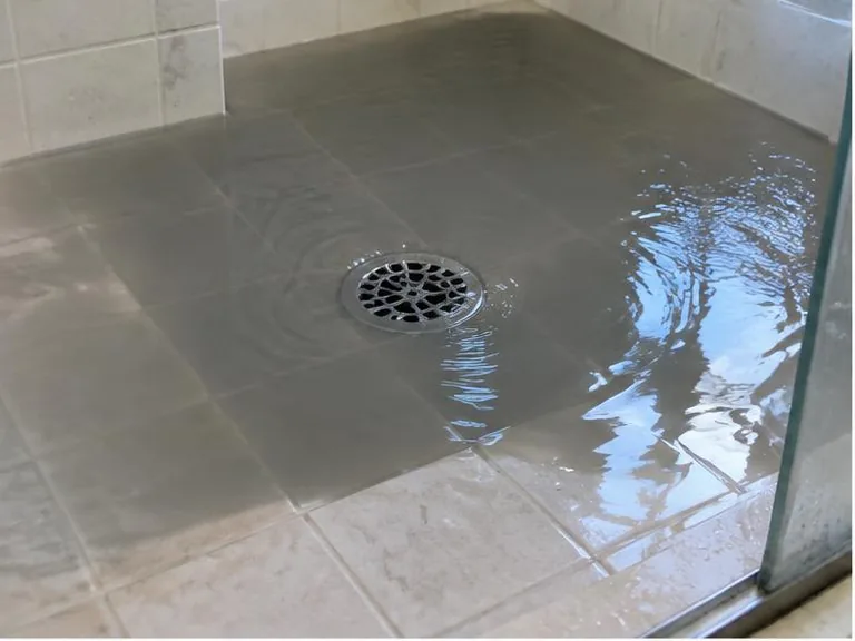 Dark water pooling around a shower floor drain.