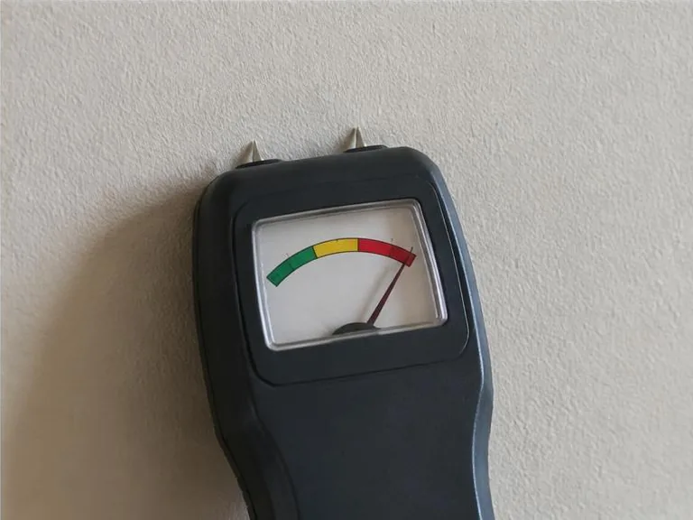 Analog moisture meter showing a high reading against a dry-looking wall.